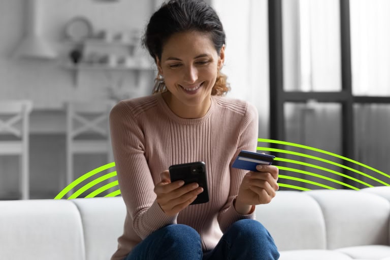 a woman sat on a sofa with a smartphone and credit card in hand
